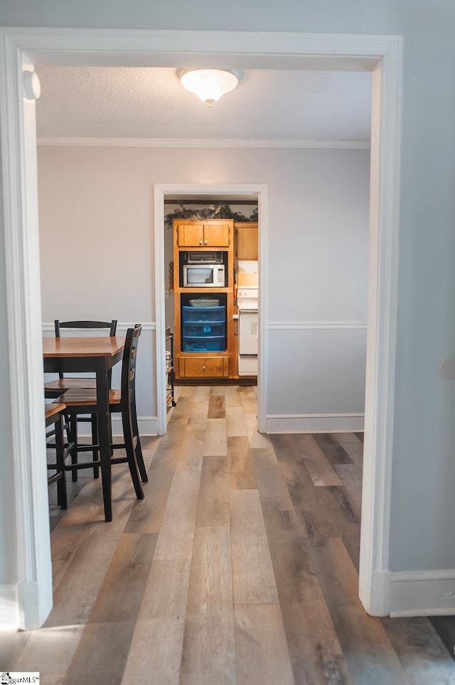 dining space featuring ornamental molding, a textured ceiling, and light wood-type flooring