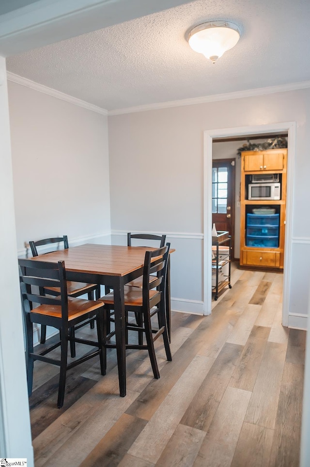 dining area with ornamental molding, light hardwood / wood-style floors, and a textured ceiling