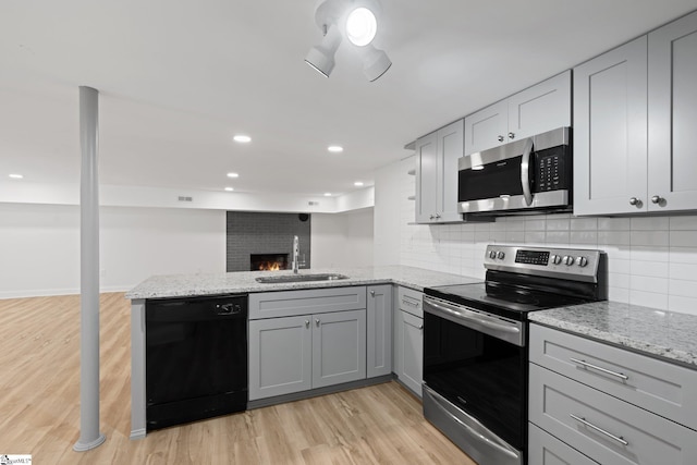 kitchen with sink, gray cabinetry, kitchen peninsula, stainless steel appliances, and light stone countertops