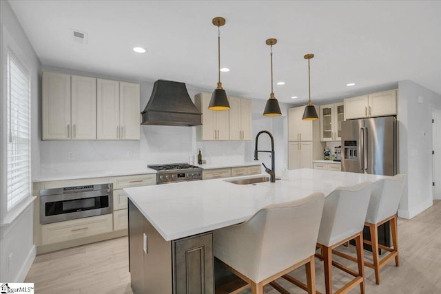 kitchen with decorative light fixtures, sink, premium appliances, a kitchen island with sink, and custom range hood