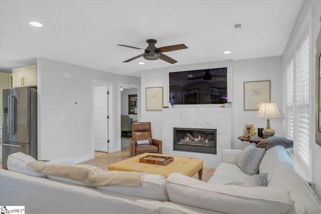 living room with ceiling fan, a fireplace, light hardwood / wood-style flooring, and a wealth of natural light