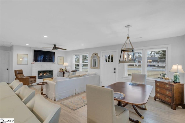 dining room featuring light hardwood / wood-style flooring, ceiling fan with notable chandelier, and a fireplace