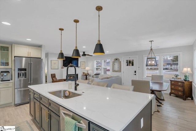 kitchen featuring sink, light stone counters, decorative light fixtures, appliances with stainless steel finishes, and an island with sink