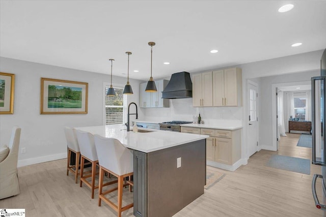 kitchen with wall chimney range hood, sink, hanging light fixtures, a kitchen breakfast bar, and a center island with sink