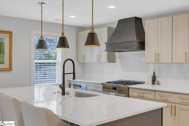 kitchen featuring sink, custom exhaust hood, hanging light fixtures, a kitchen island with sink, and high end stove