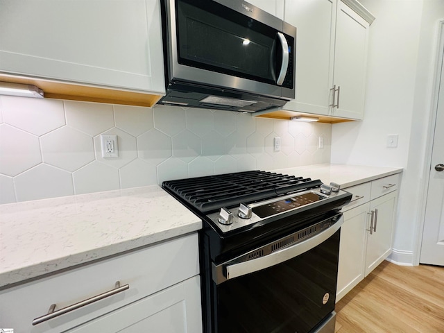 kitchen featuring white cabinetry, light stone counters, light wood-type flooring, gas range oven, and backsplash