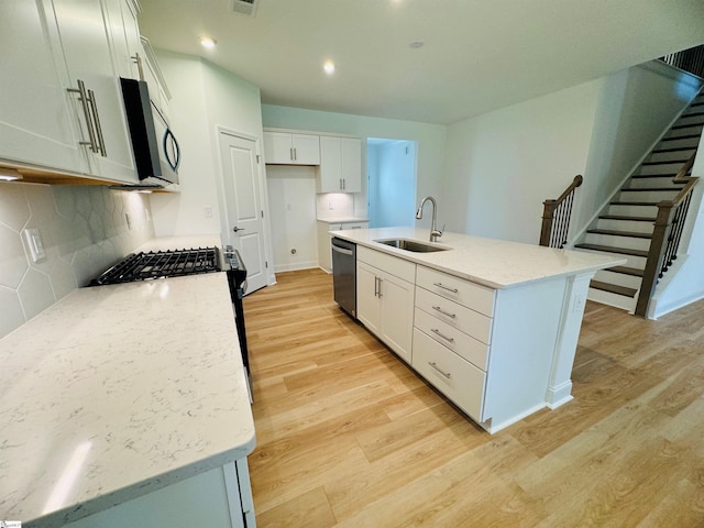 kitchen featuring sink, dishwasher, a kitchen island with sink, white cabinetry, and light stone countertops