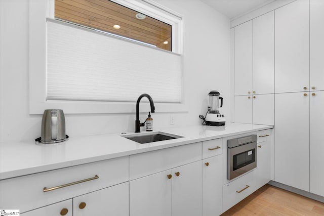 kitchen featuring stainless steel microwave, sink, light hardwood / wood-style flooring, and white cabinets