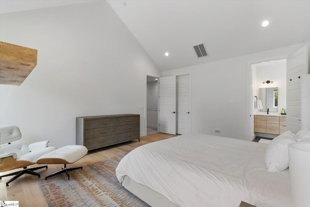 bedroom with high vaulted ceiling, light hardwood / wood-style floors, and ensuite bath