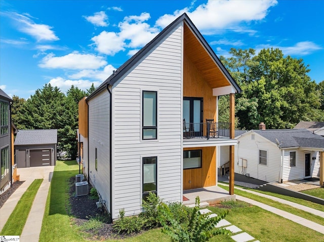 rear view of property featuring a balcony, an outbuilding, a garage, a yard, and central AC