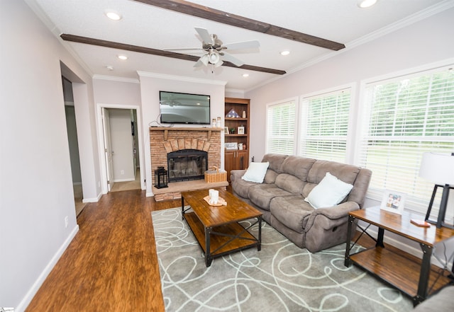 living room featuring crown molding, ceiling fan, hardwood / wood-style floors, beam ceiling, and a stone fireplace