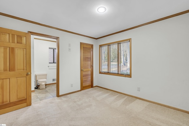 unfurnished bedroom with crown molding, a closet, ensuite bath, and light carpet