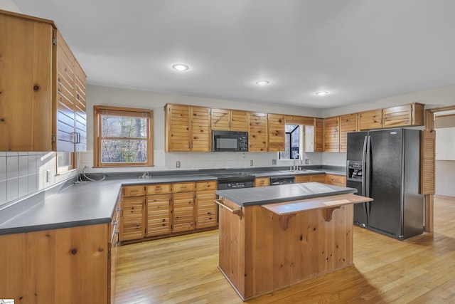 kitchen with sink, a center island, black appliances, decorative backsplash, and light wood-type flooring