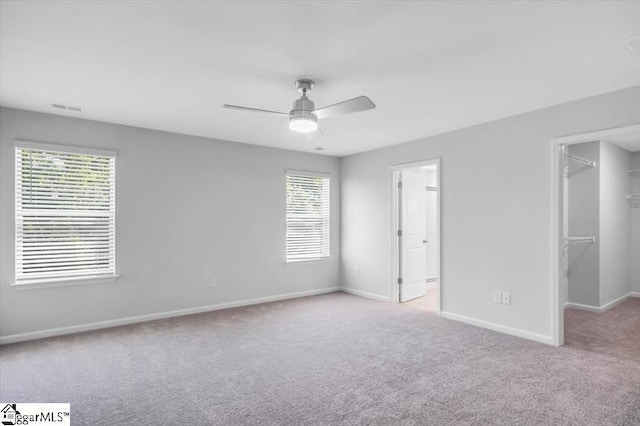 unfurnished bedroom with multiple windows, a walk in closet, and light colored carpet