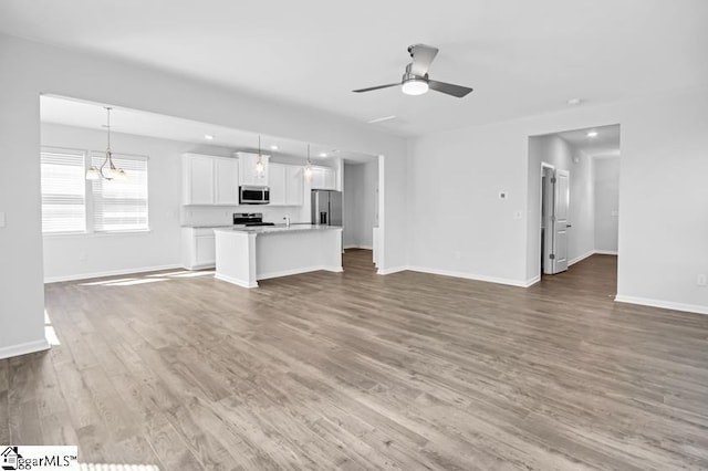 unfurnished living room with a ceiling fan, baseboards, recessed lighting, and wood finished floors