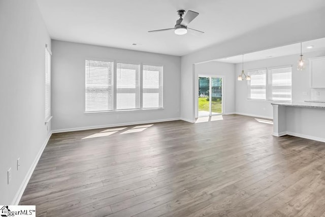 unfurnished living room featuring baseboards, ceiling fan, and dark wood-style flooring