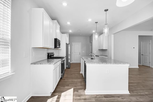 kitchen with appliances with stainless steel finishes, white cabinetry, light stone counters, a center island with sink, and decorative light fixtures