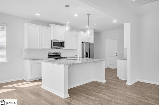 kitchen with appliances with stainless steel finishes, sink, white cabinets, light stone counters, and a center island with sink