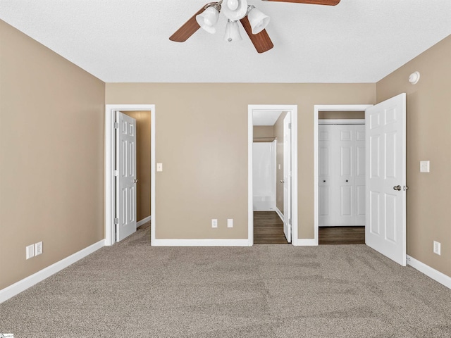 unfurnished bedroom featuring dark colored carpet, a closet, ceiling fan, and ensuite bath