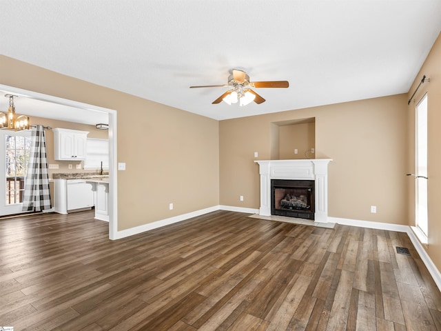 unfurnished living room with sink, a healthy amount of sunlight, dark hardwood / wood-style floors, and ceiling fan with notable chandelier