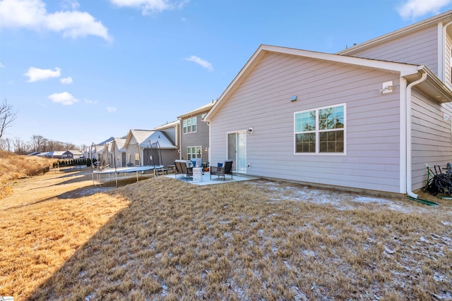 rear view of property with a patio, a trampoline, and a lawn