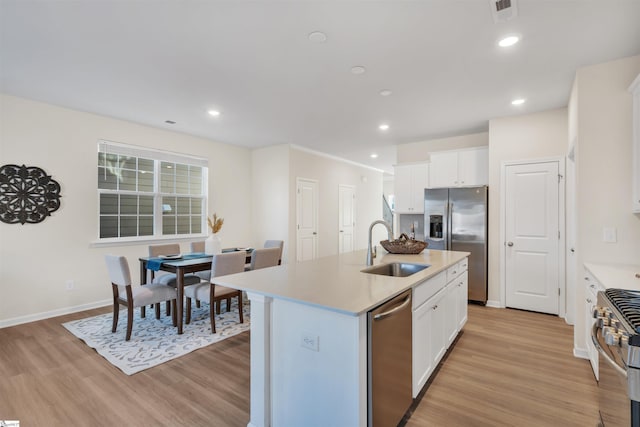 kitchen with an island with sink, white cabinetry, sink, light hardwood / wood-style floors, and stainless steel appliances