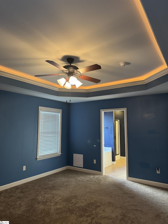 spare room with a raised ceiling, light colored carpet, and ceiling fan