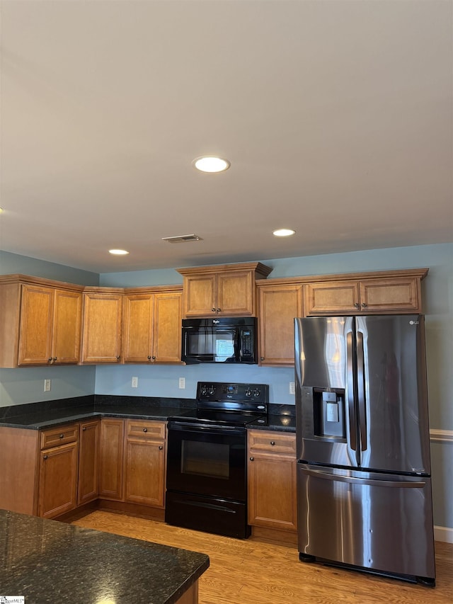 kitchen with dark stone countertops, light hardwood / wood-style flooring, and black appliances