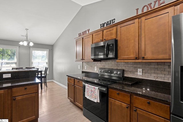 kitchen featuring lofted ceiling, appliances with stainless steel finishes, dark stone countertops, hanging light fixtures, and tasteful backsplash