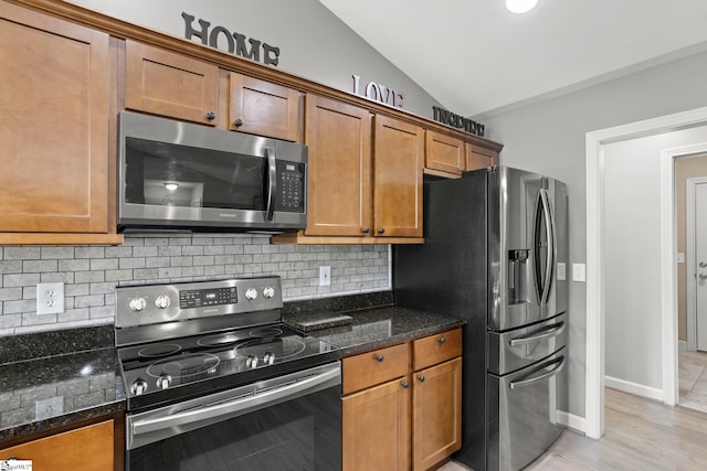 kitchen with appliances with stainless steel finishes, tasteful backsplash, lofted ceiling, dark stone counters, and light hardwood / wood-style floors