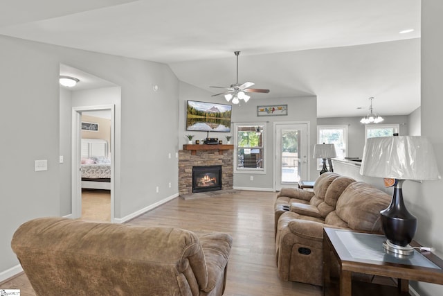 living room featuring ceiling fan, a fireplace, vaulted ceiling, and light wood-type flooring