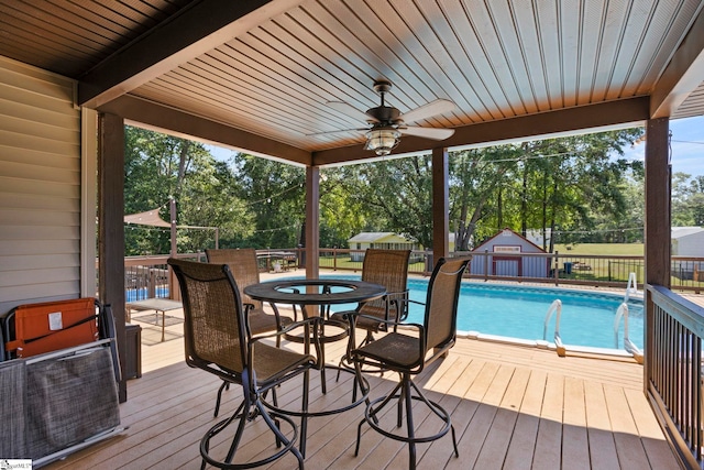 wooden deck featuring ceiling fan, an outdoor structure, and a fenced in pool