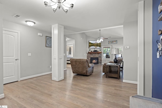 living room featuring a fireplace, ceiling fan with notable chandelier, and light hardwood / wood-style flooring