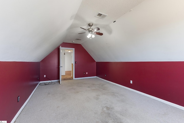 additional living space featuring lofted ceiling, ceiling fan, light colored carpet, and a textured ceiling