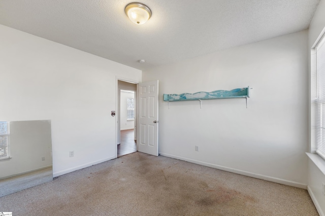 unfurnished room featuring a textured ceiling, light carpet, and a wealth of natural light