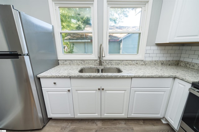 kitchen featuring stainless steel refrigerator, white cabinetry, light stone countertops, and sink