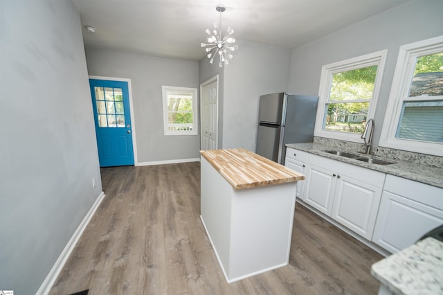 kitchen with sink, a center island, hanging light fixtures, stainless steel refrigerator, and white cabinets