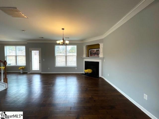 312 Engelmann Ln, Simpsonville, SC 29680 - unfurnished living room with crown molding, plenty of natural light, an inviting chandelier, and dark hardwood / wood-style flooring