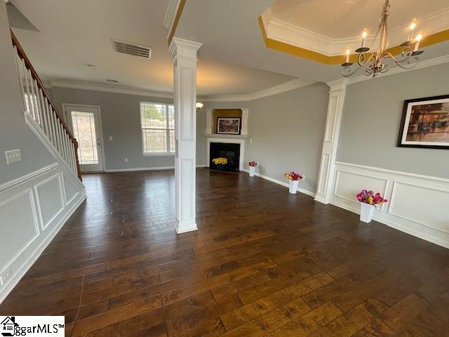 312 Engelmann Ln, Simpsonville, SC 29680 - unfurnished living room featuring ornate columns, ornamental molding, dark hardwood / wood-style floors, a tray ceiling, and a notable chandelier