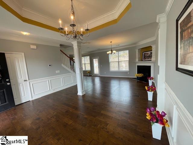 312 Engelmann Ln, Simpsonville, SC 29680 - unfurnished living room featuring dark wood-type flooring, a tray ceiling, ornamental molding, a chandelier, and ornate columns