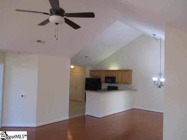 unfurnished living room with dark hardwood / wood-style flooring, ceiling fan with notable chandelier, and vaulted ceiling