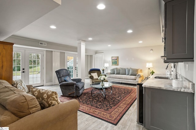 living room featuring sink, light hardwood / wood-style floors, french doors, and decorative columns