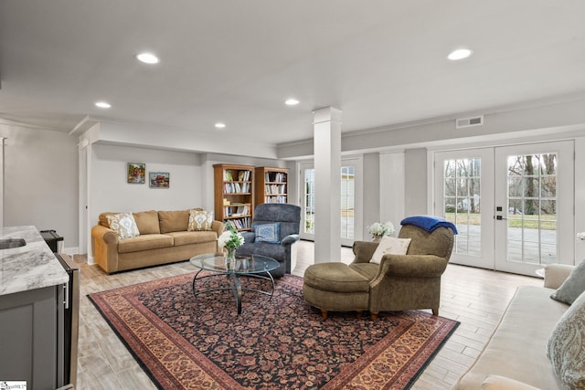 living room featuring french doors, crown molding, decorative columns, and light wood-type flooring