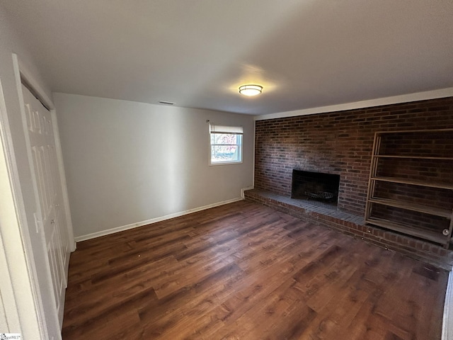 unfurnished living room featuring a brick fireplace and dark hardwood / wood-style floors