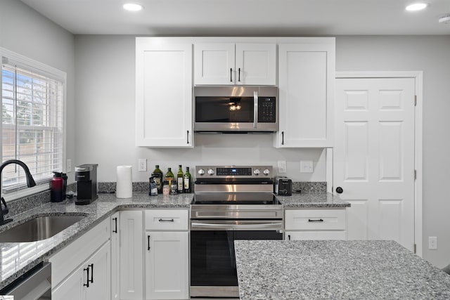 kitchen with stainless steel appliances, sink, white cabinets, and light stone counters