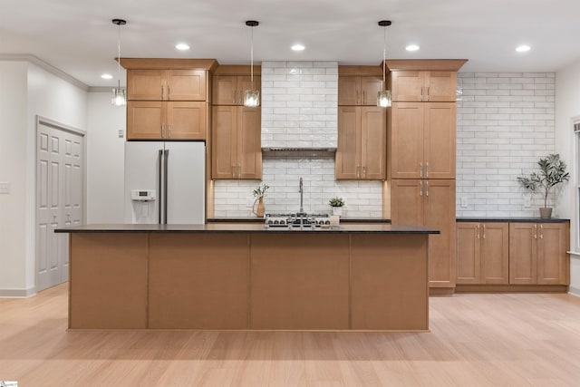 kitchen with hanging light fixtures, white fridge with ice dispenser, a kitchen island with sink, and light hardwood / wood-style flooring