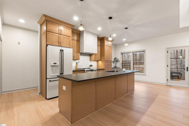 kitchen featuring decorative backsplash, white fridge with ice dispenser, a center island with sink, decorative light fixtures, and wall chimney exhaust hood