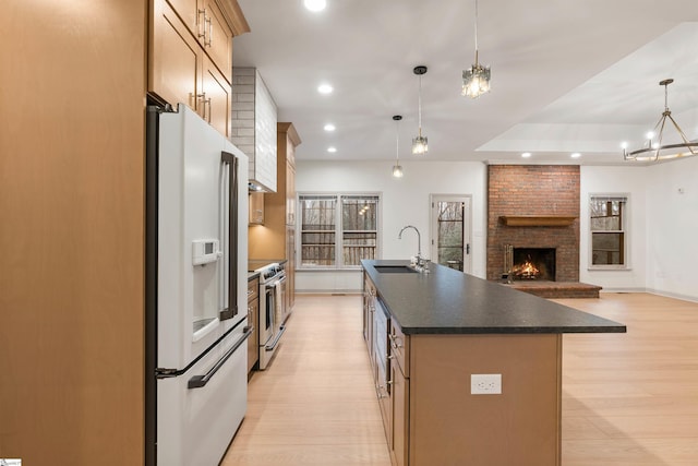 kitchen featuring pendant lighting, stainless steel stove, sink, white fridge with ice dispenser, and a large island