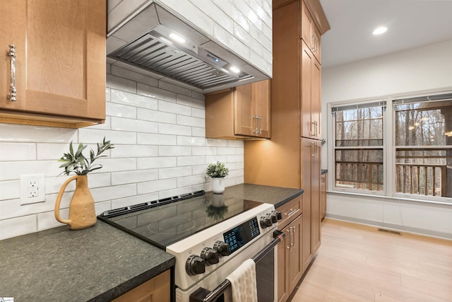 kitchen featuring wall chimney range hood, backsplash, light hardwood / wood-style floors, and stainless steel electric range oven