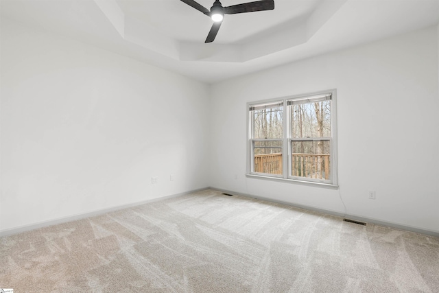 carpeted empty room with ceiling fan and a raised ceiling